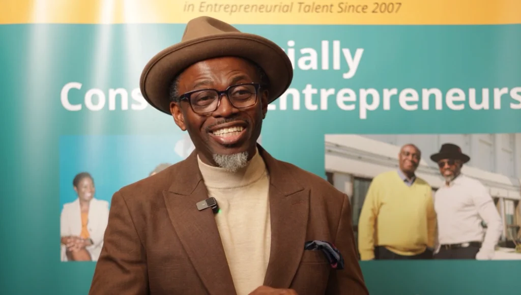 Charismatic speaker Tony Dada wearing a hat and suit, smiling confidently with a microphone at the Socially Conscious Entrepreneur Conference