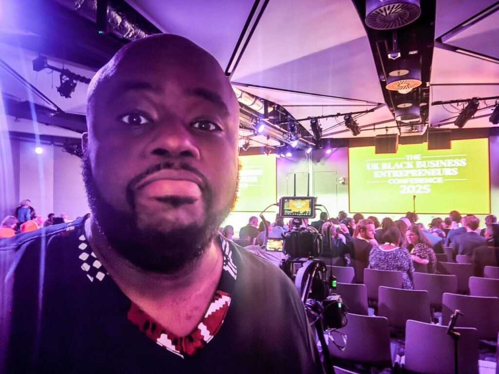 Bald Black man with beard taking a selfie in front of the stage at the UK Black Business Entrepreneurs Conference 2025